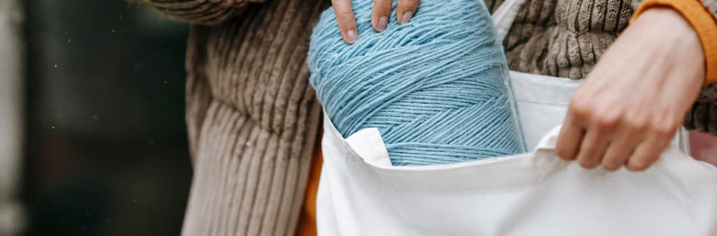 Hands placing yarn into a reusable tote bag
